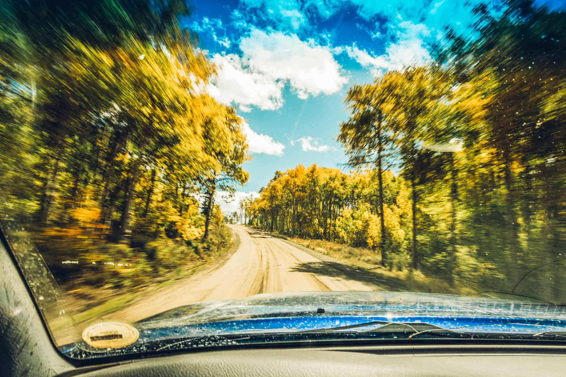 A car driving down a dirt road with trees in the background.