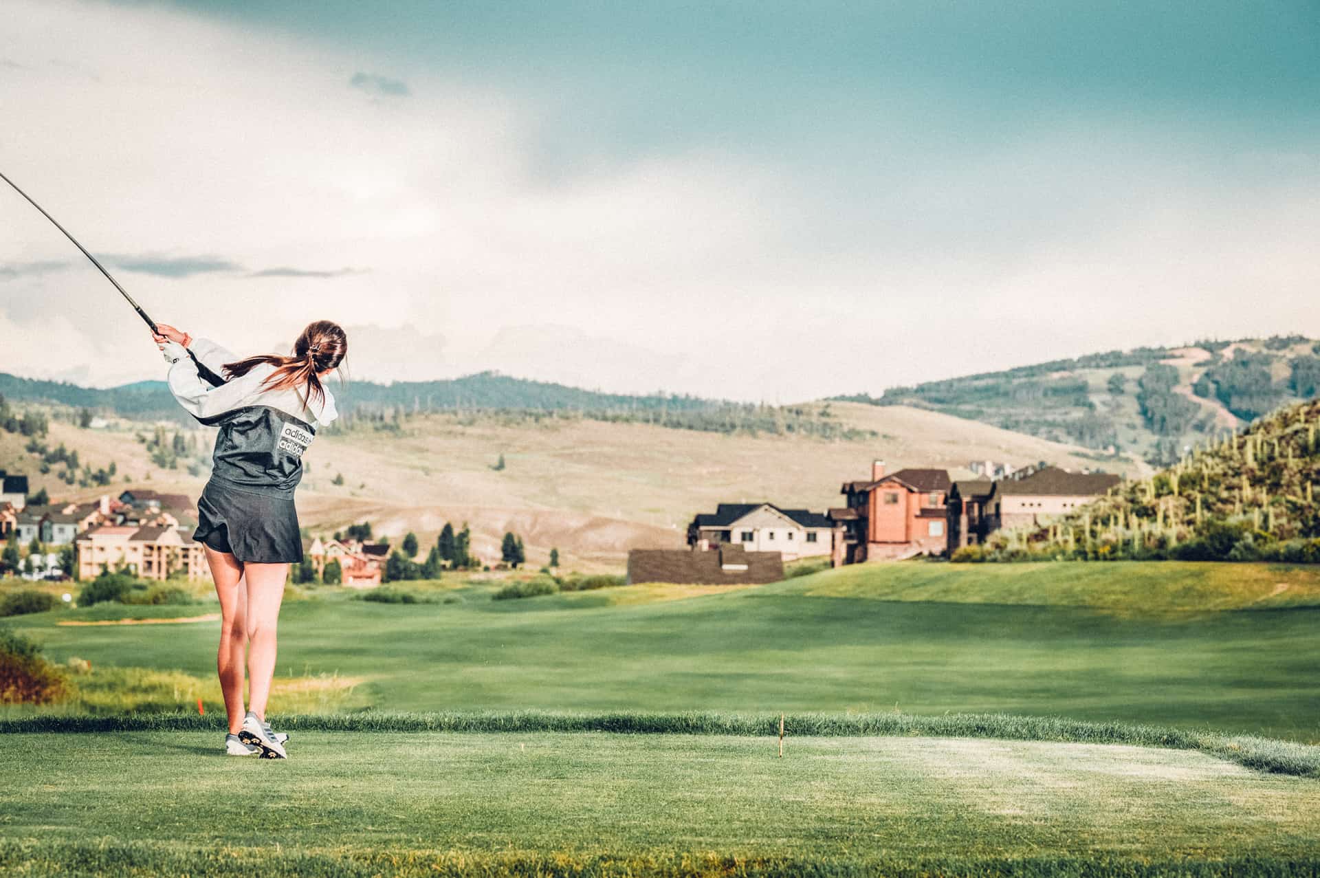 A woman is playing golf on a golf course with mountains in the background.