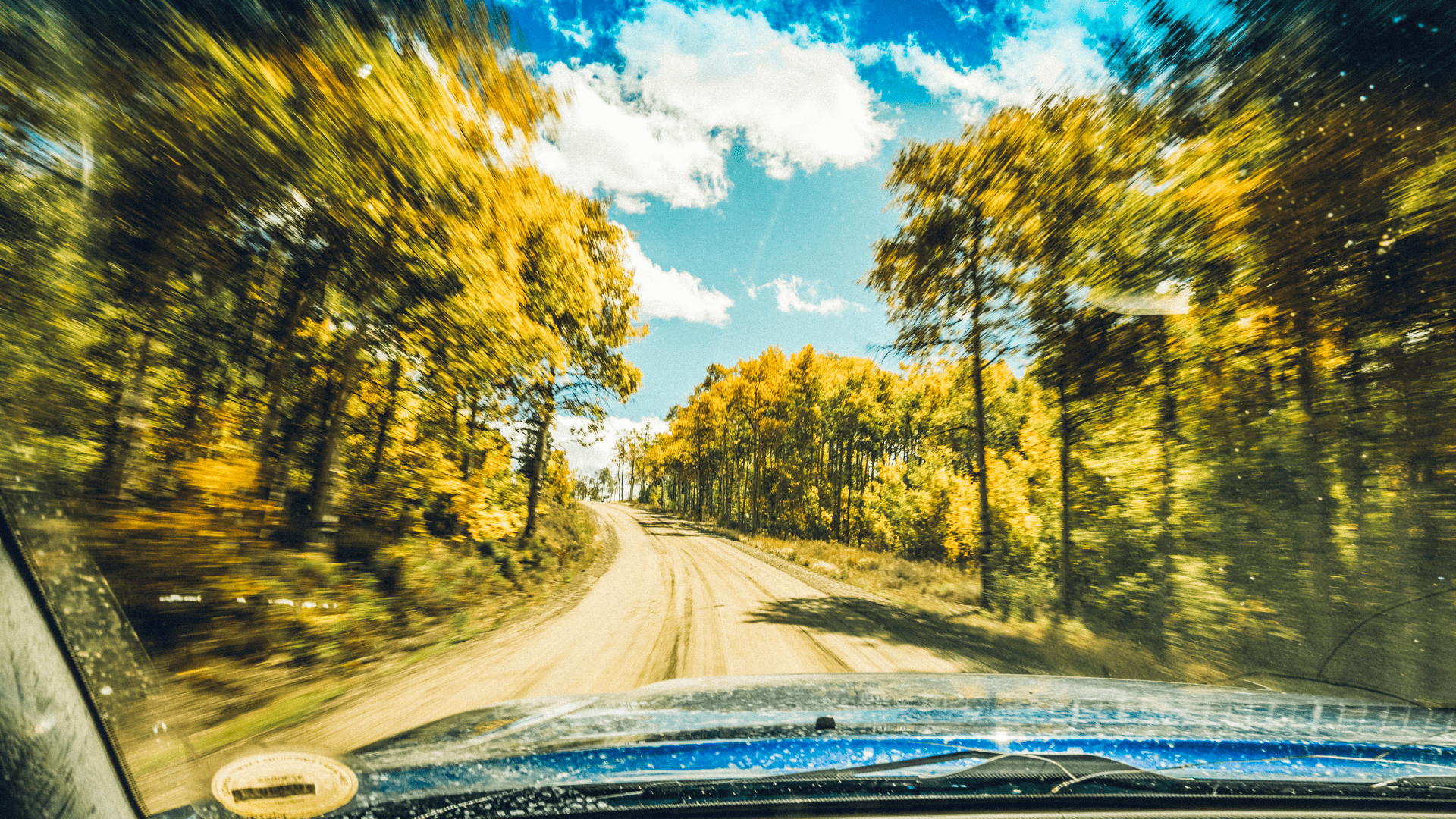 A car driving down a dirt road with trees in the background.