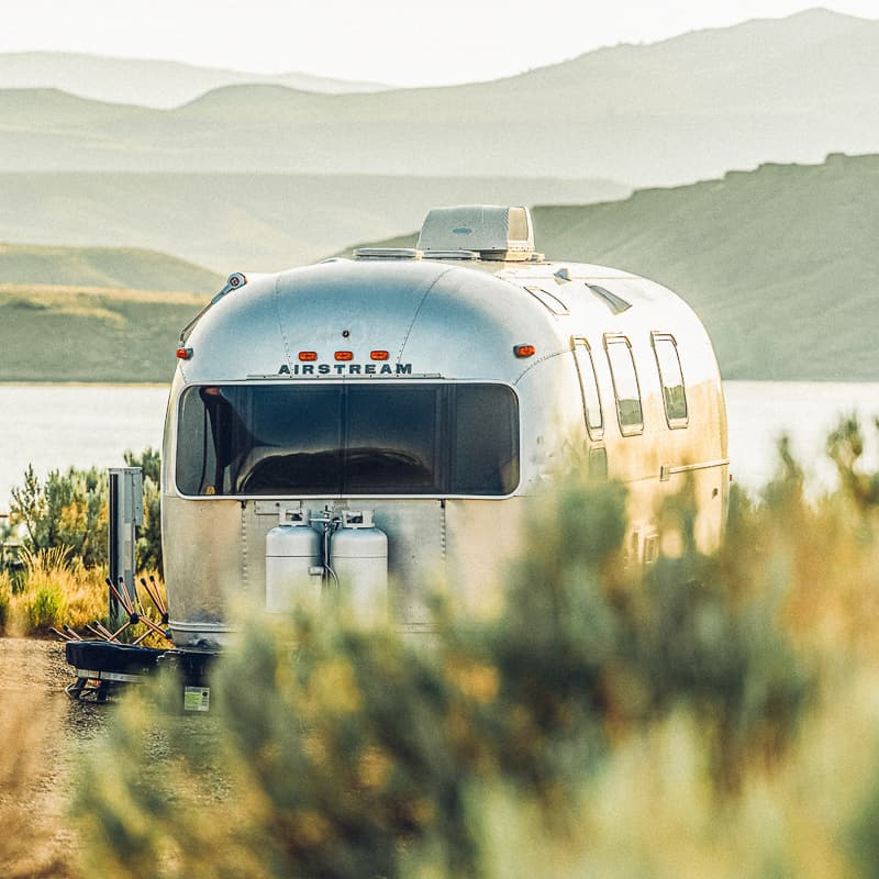 A silver airstream parked next to a lake.