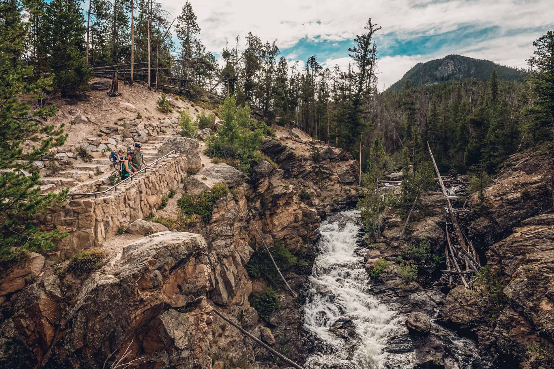 A couple walking down a rocky path next to Adams Falls in Rocky Mountain National Park