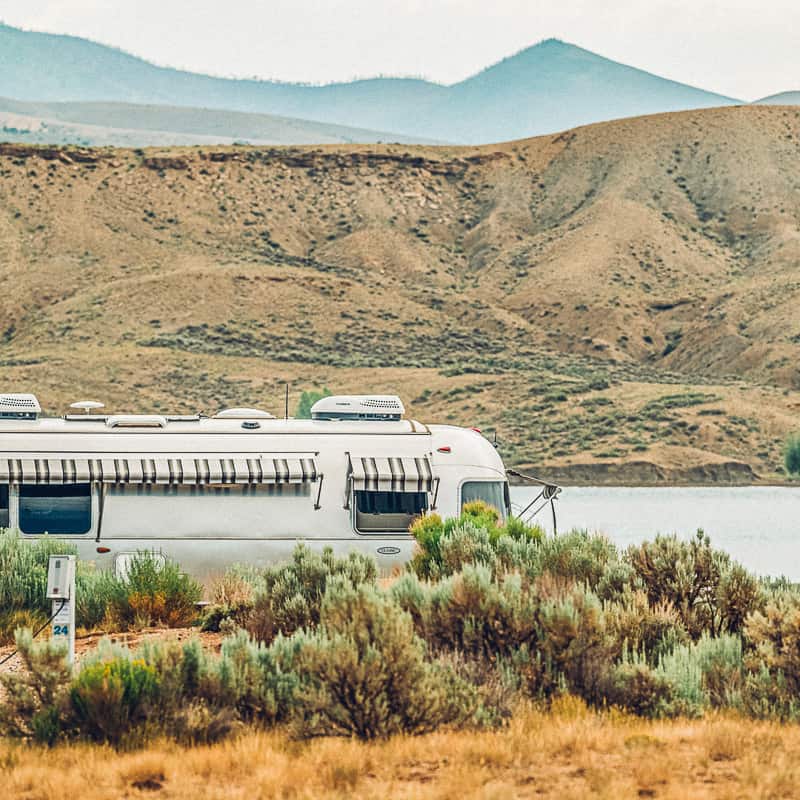 An airstream parked next to a lake with mountains in the background.