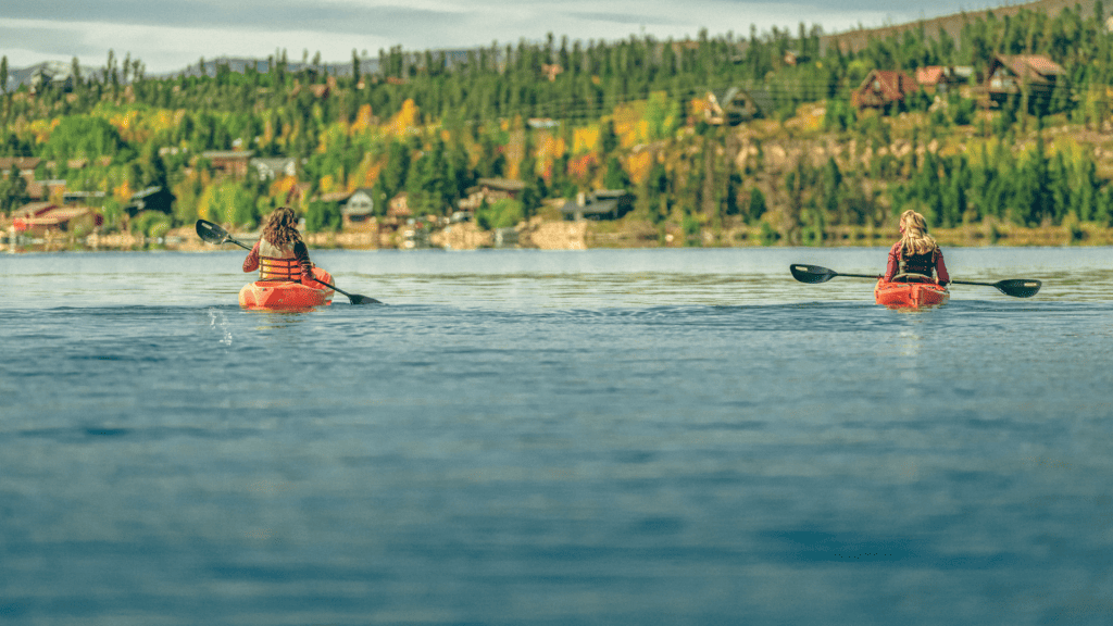 Two people paddling kayaks on a lake with trees in the background.