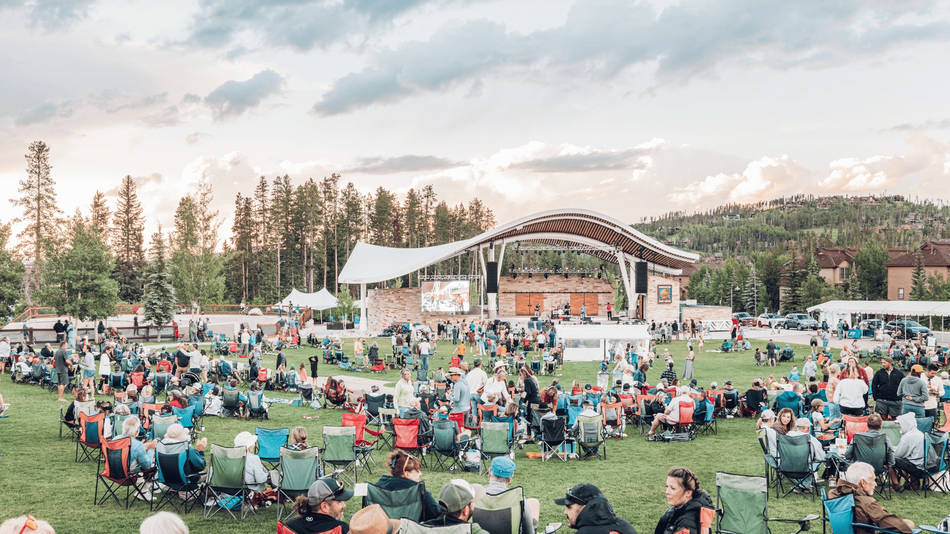 A crowd of people sitting in lawn chairs at an outdoor concert.