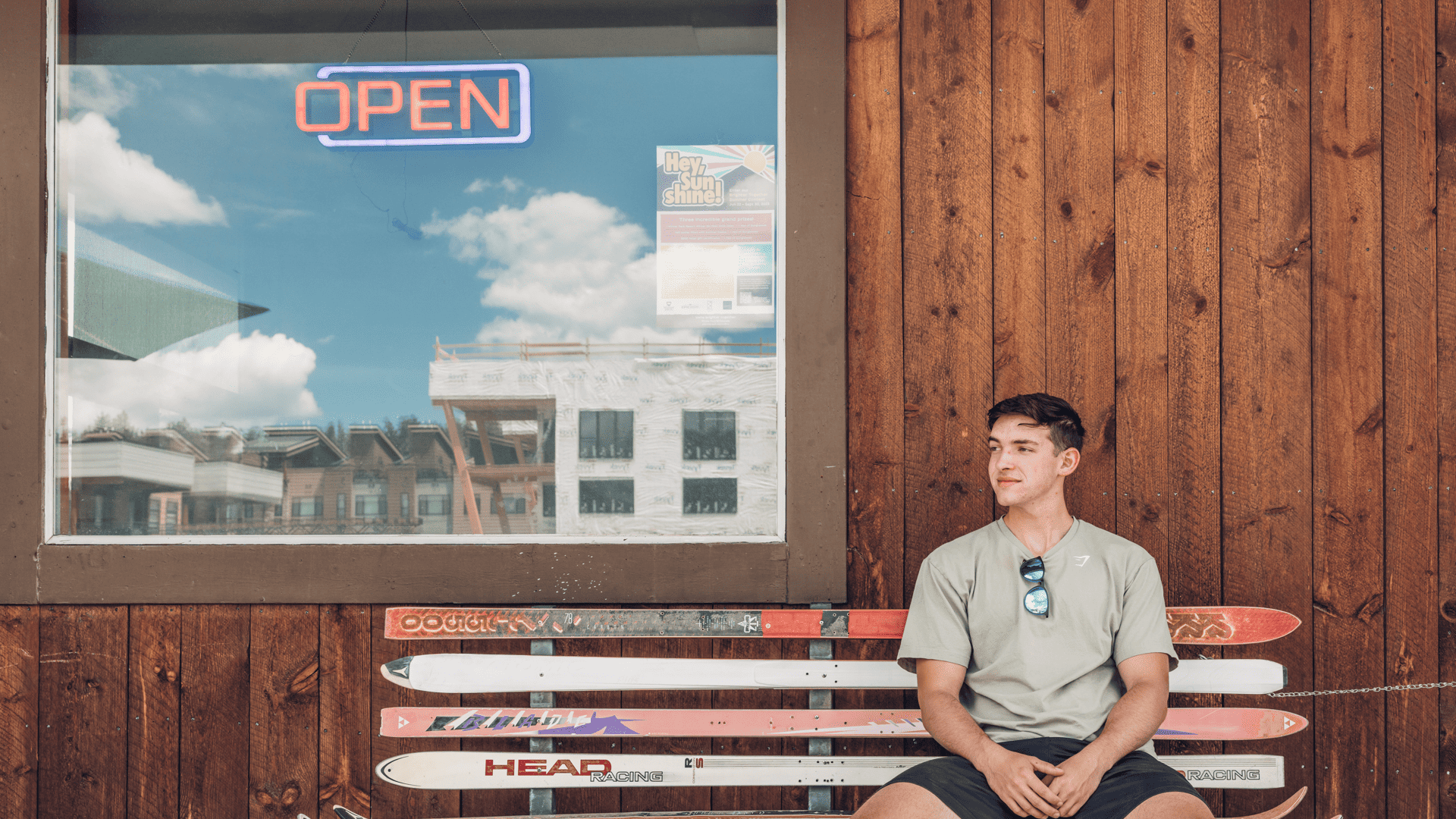 A young man sitting on a bench next to some skis.