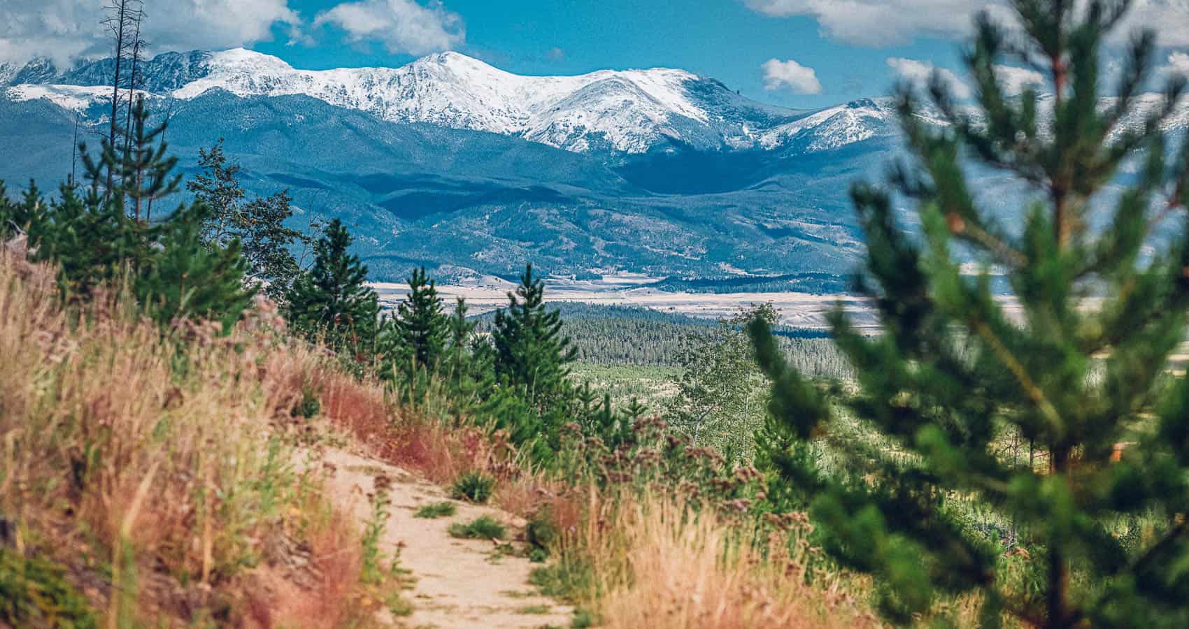 A trail leading to a mountain with snow capped mountains in the background.