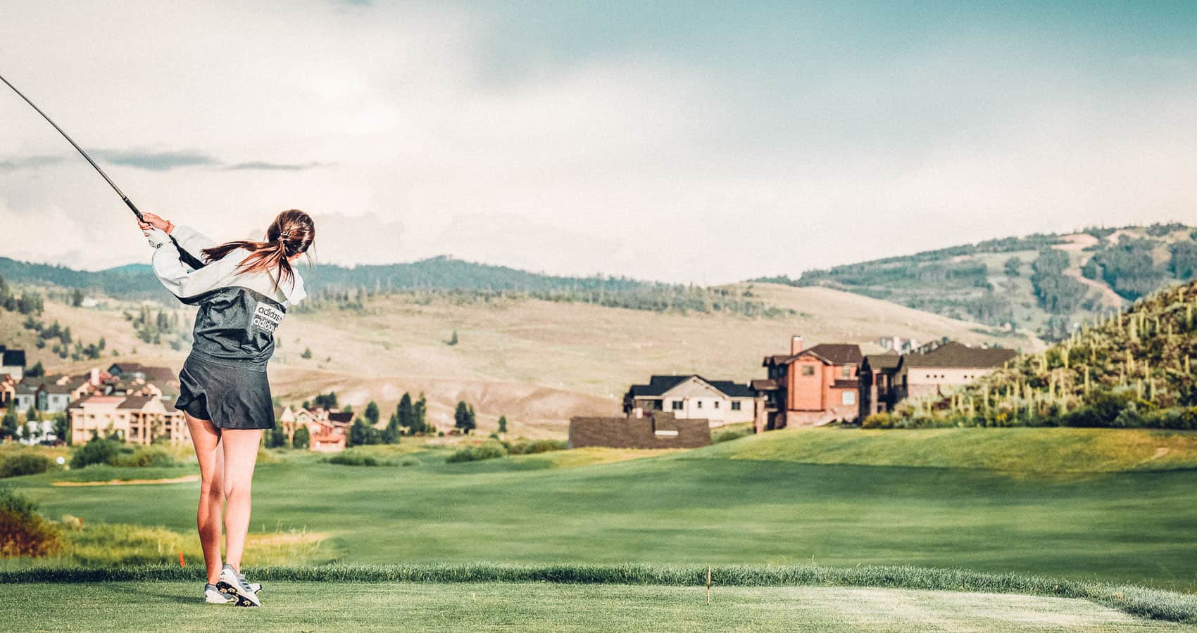 A woman is playing golf on a golf course with mountains in the background.