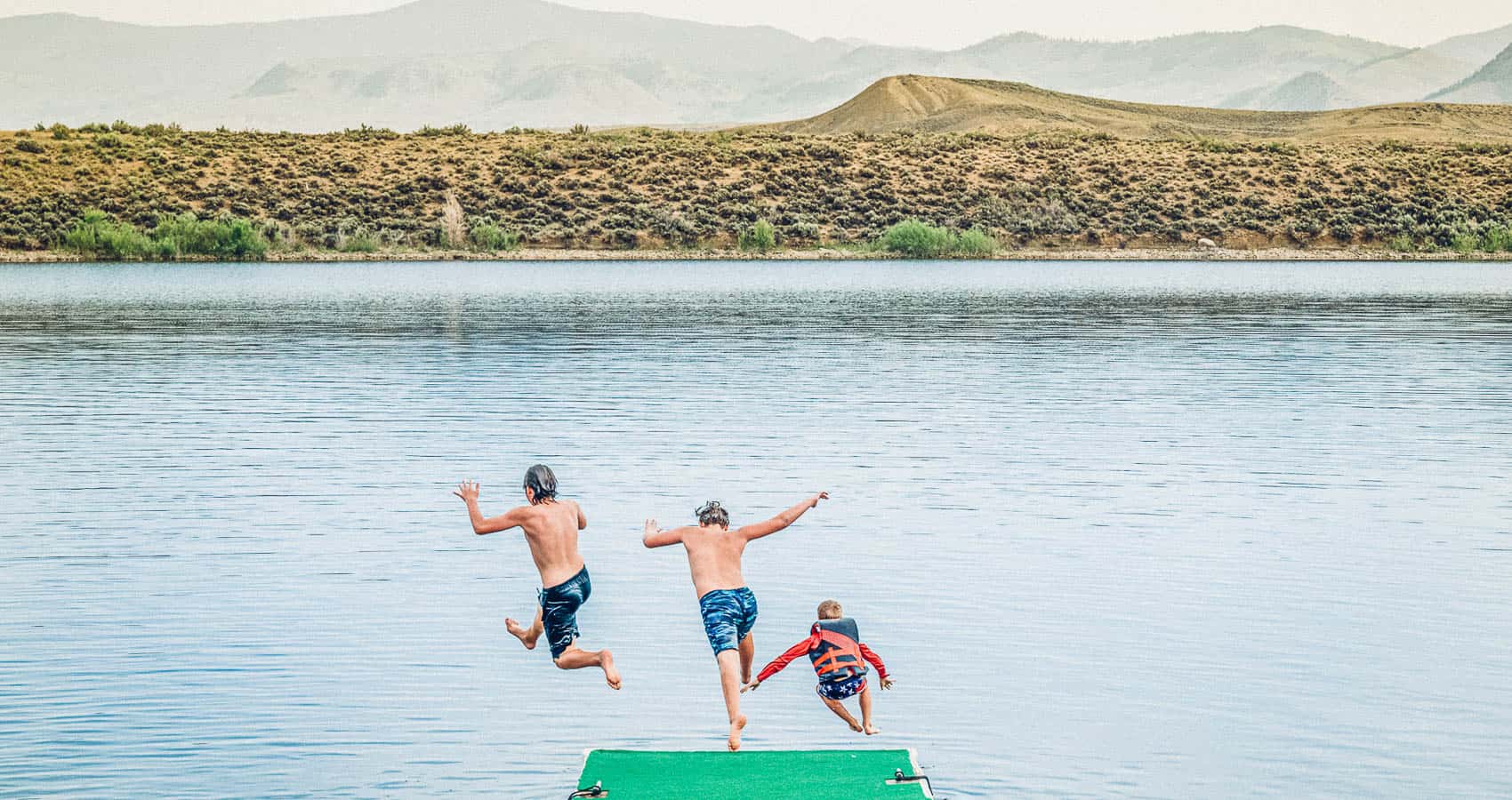 Three people jumping off a dock into a lake.