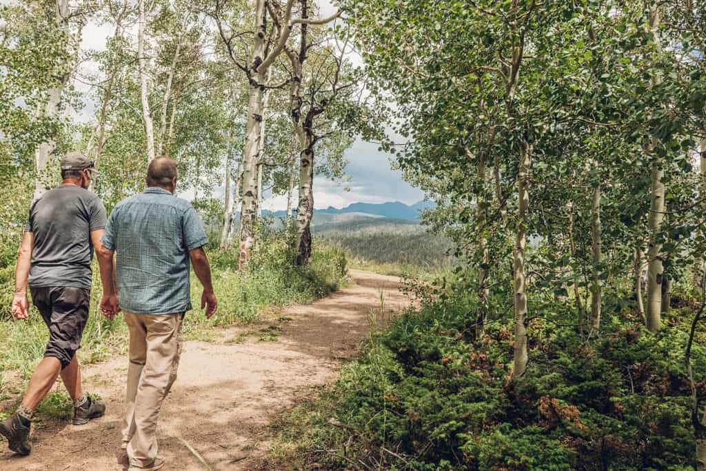 Two men walking down a trail with trees in the background.