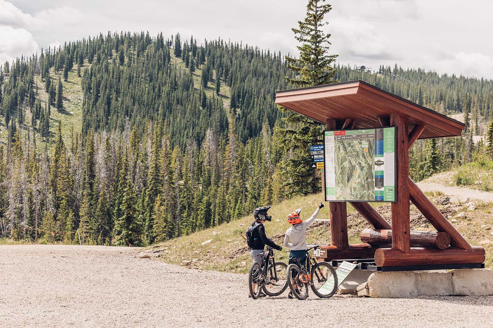 Two people standing next to a sign at the top of a mountain.