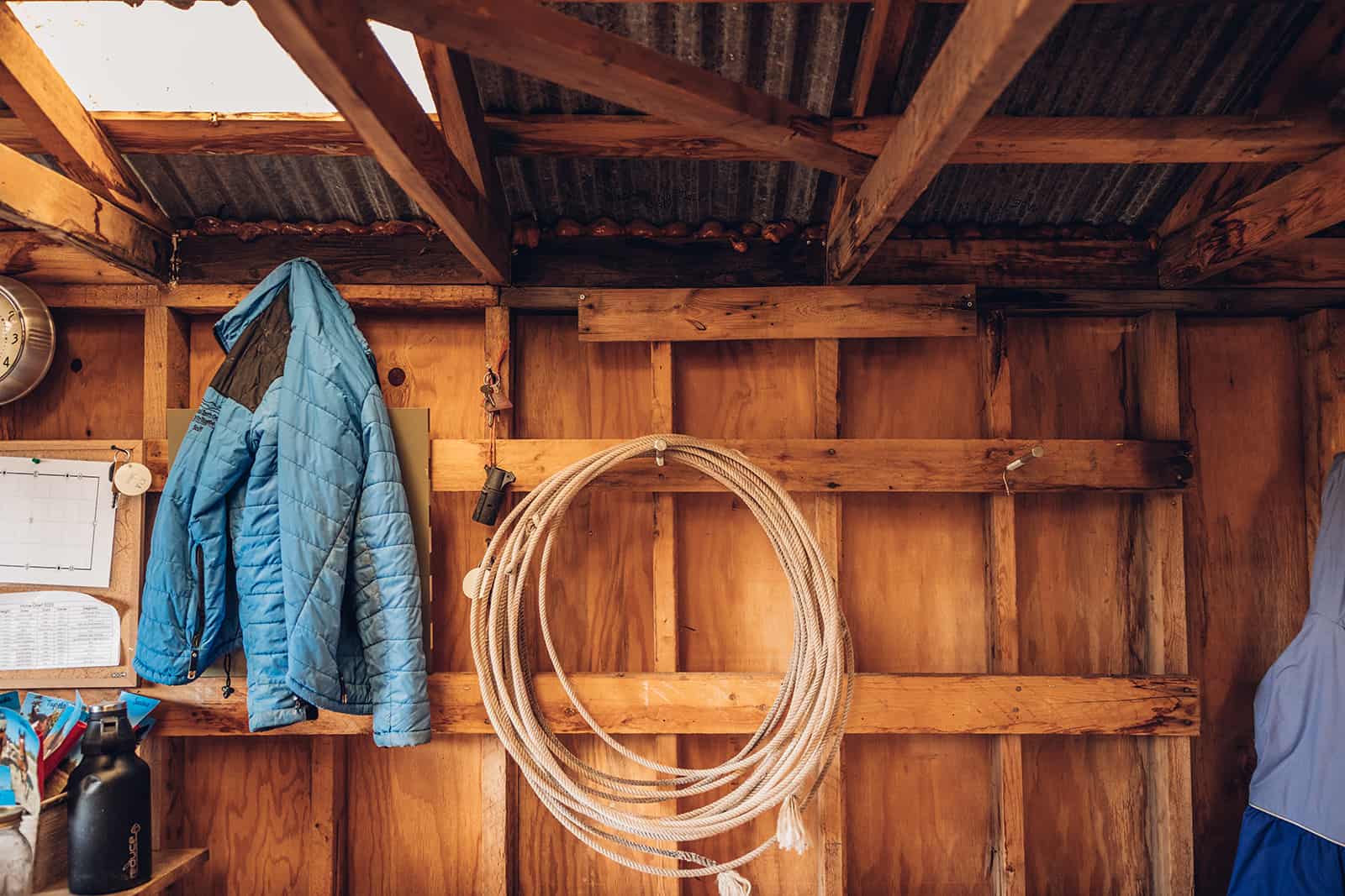 A blue jacket hangs on a hook in a barn.