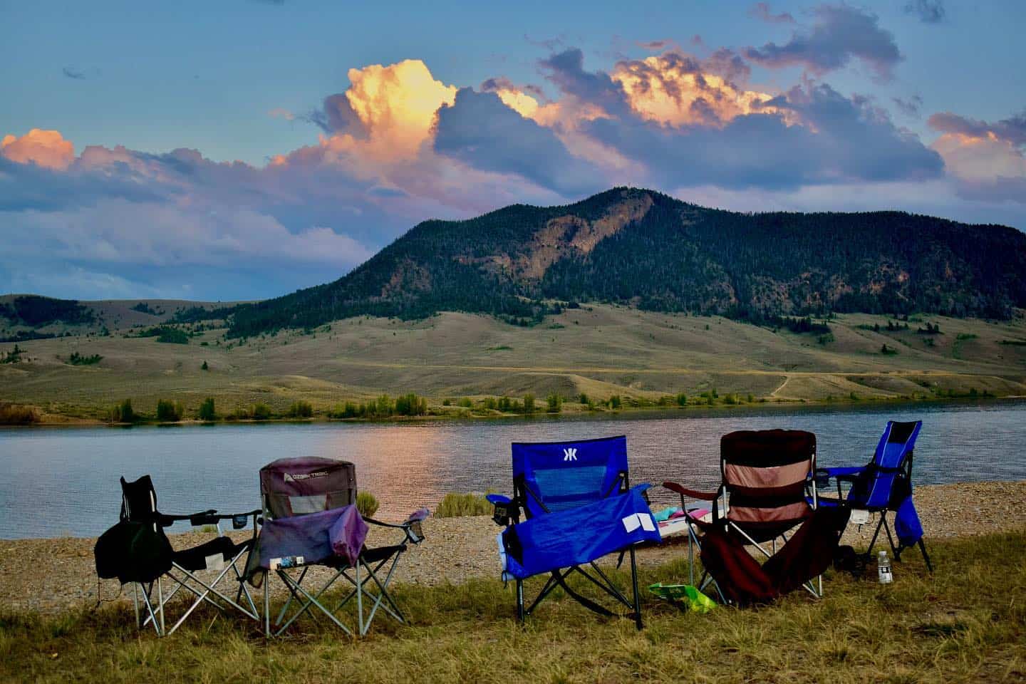 A group of camping chairs in front of a lake with mountains in the background.