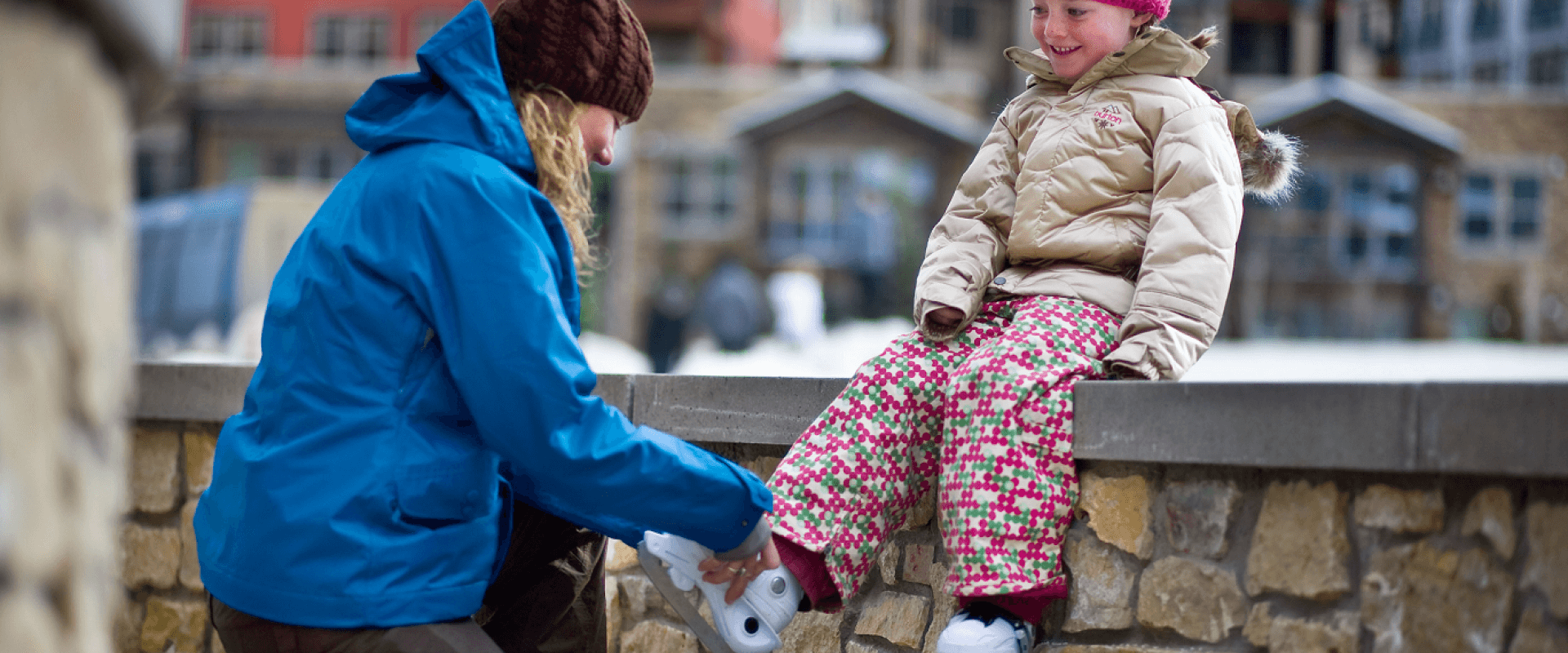 A woman is helping a little girl put on her ski boots.