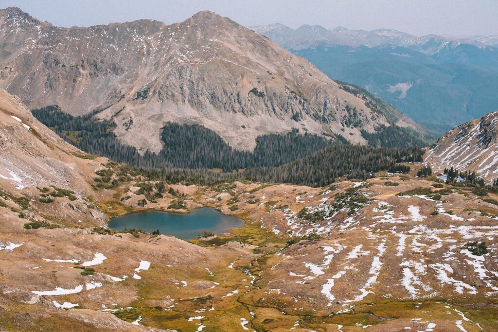 An aerial view of a lake in a mountain valley, with traces of snow remaining on the valley floor.