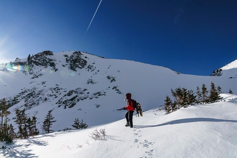 A person hiking up a snow covered mountain with the sun behind them.