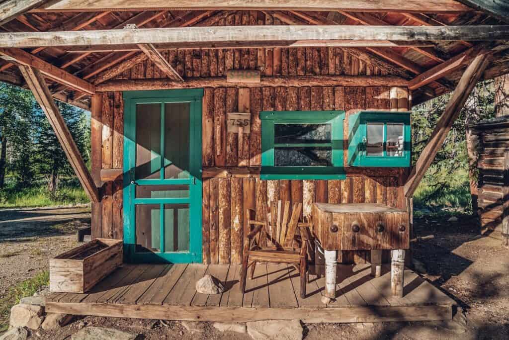 Rustic wooden cabin with a turquoise door and window frames, exuding a vintage frontier charm.