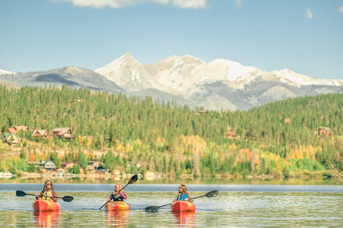 Three people kayak on Grand Lake with Rocky Mountain National Park peaks in the background