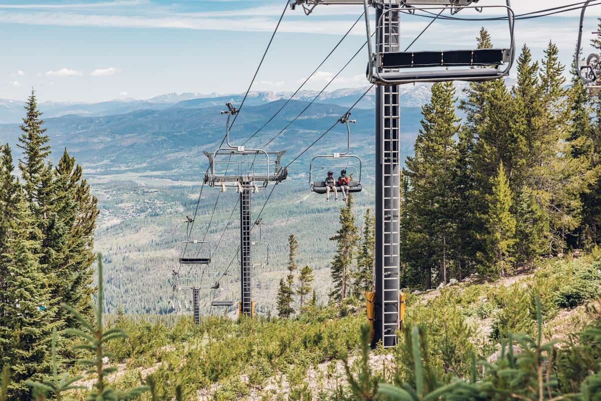 People ride on a ski life on a summer day with the Continental Divide in the background.