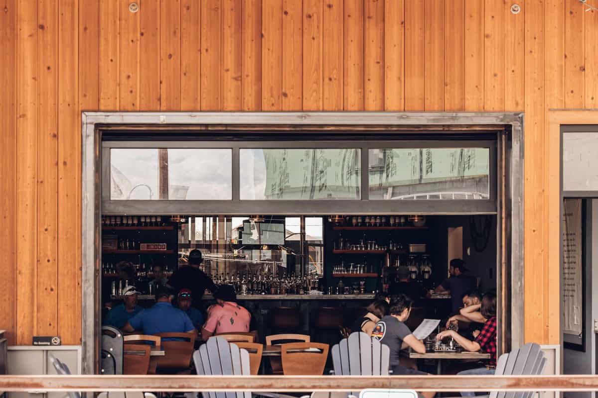 A group of people seated at a bar inside a restaurant in Fraser, Colorado. The bar is seen through an open window or doorway.