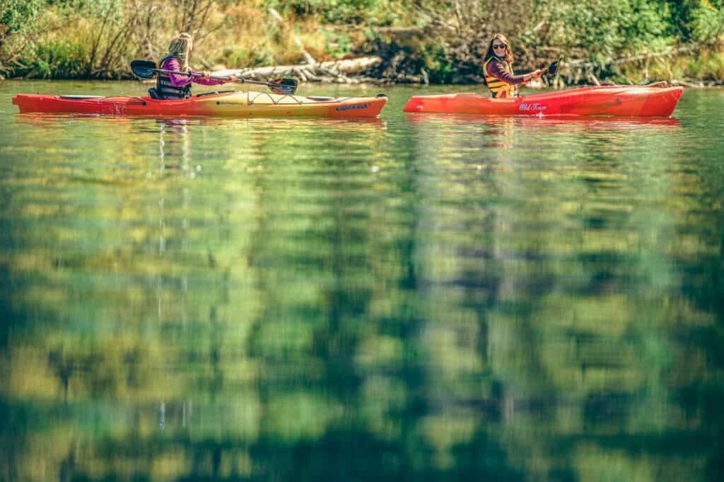 Two people smile as they kayak on Grand Lake with green trees in the background