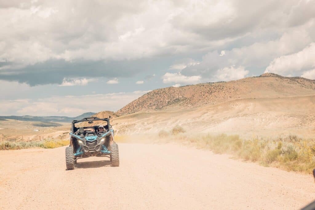 An ATV rides on a dirt path with dust in the air. Mountains are in the background in Kremmling. 