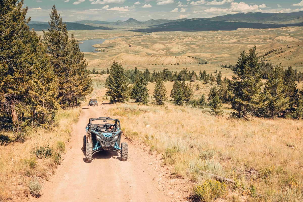 Two ATVs ride up a trail in Kremmling with plateaus, mountains and a reservoir in the background 