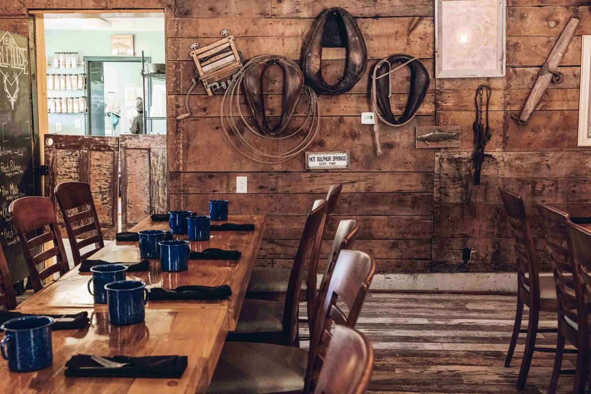 Interior of restaurant in Hot Sulphur Springs, Dean Public House. A wood table is set with blue mugs, napkins and silverware with lassos on the wall in the background.