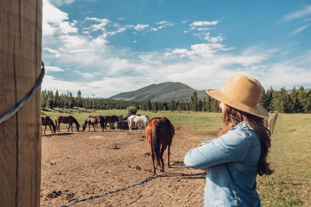 A person wearing a straw hat looks at horses at Snow Mountain Ranch / YMCA of the Rockies in Granby, a popular camping spot in Grand County