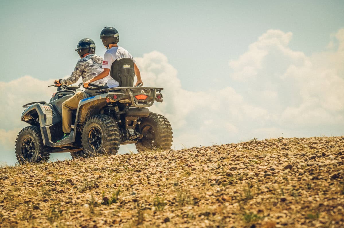 Two individuals riding an all-terrain vehicle (ATV) on rocky terrain under a clear sky on Stillwater Pass.