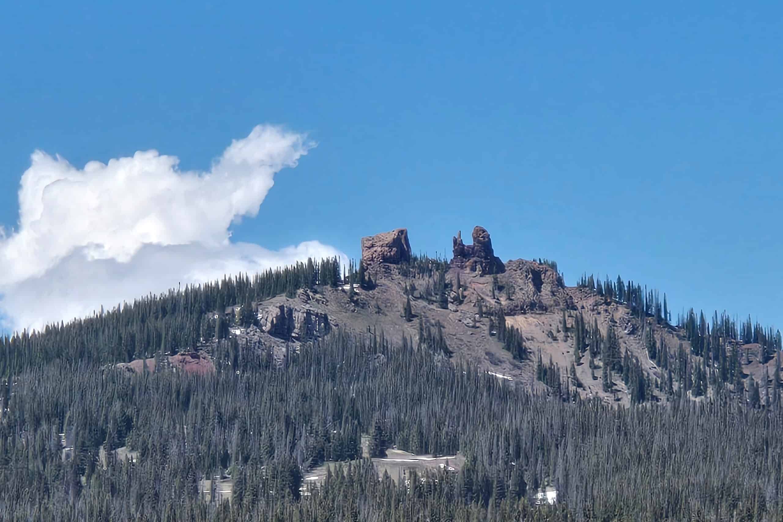 The rabbit-ears shaped rock spires protrude from trees at the summit of Rabbit Ears Pass with a clear blue sky and a single white cloud.